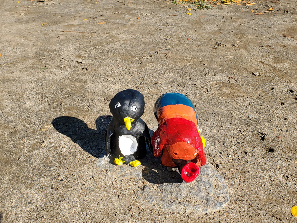 Sculpture de pingouin et sculpture d’éléphant multicolore sur une pierre entourée de sable