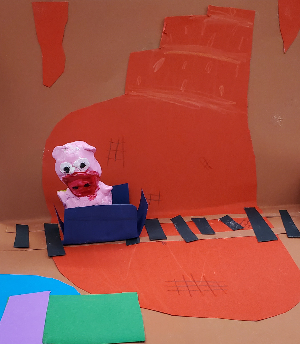 Oeuvre d'enfant. Figurine d’animal inventé ressemblant à un cochon, placée dans un wagon de carton sur un arrière-plan de grotte avec des rails, réalisé en collage et dessin.