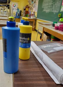 Des bouteilles de peinture acrylique sur une table, dans une salle de cours